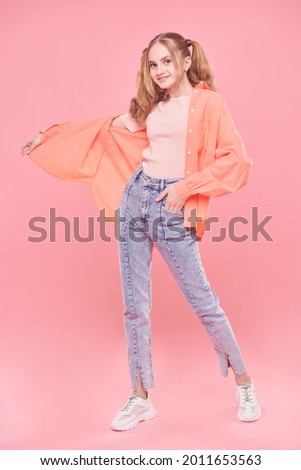 Teenage style. Full length portrait of a pretty teenage girl in bright summer clothes and with ponytails smiling at camera. Pink background.