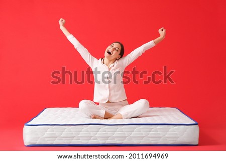 Happy young woman sitting on mattress against color background Royalty-Free Stock Photo #2011694969