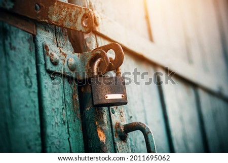 An old rusty lock hangs on the abandoned wooden gate, painted blue, which closes them and is illuminated by sunlight. Secret.