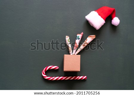 Banknotes in a Christmas package, a sugar cane and a red Santa hat. Flat lay, picture background. 
