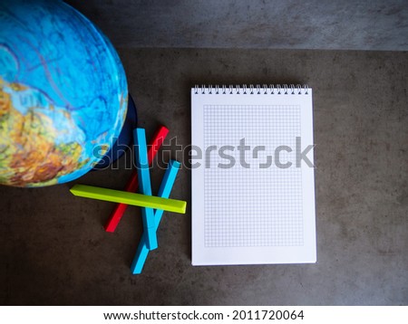 A globe, a notebook, and colored ballpoint pens lie on a gray concrete table.