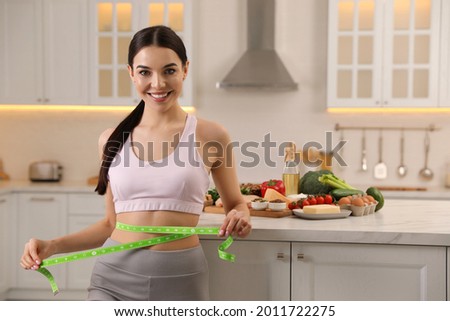 Happy woman measuring waist with tape in kitchen. Keto diet Royalty-Free Stock Photo #2011722275