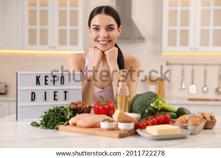 Happy woman near lightbox with words Keto Diet and different products in kitchen