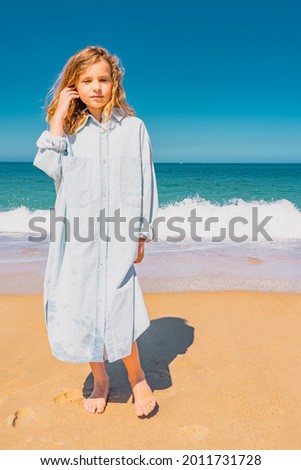 Young beautiful girl in blue dress staying along the sandy beach near the waves. High quality photo