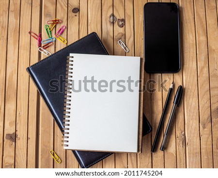 Empty Opened Journal Beside Mobile With Pens On Top Of Wooden Desk. Blank Spiral Notebook Pad Alongside A Phone With Ballpens Placed On A Table. Royalty-Free Stock Photo #2011745204