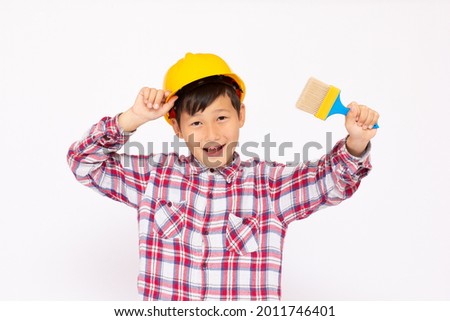 Little kid as a construction worker wearing yellow helmet with a paintbrush in his hand..White background studio picture.