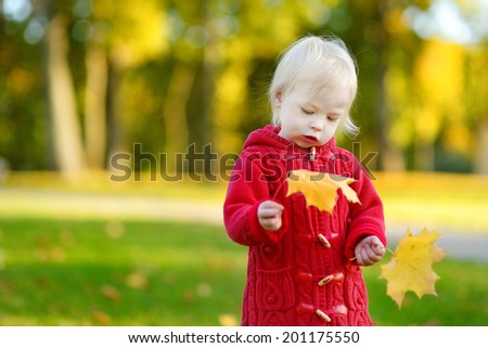 Adorable toddler girl holding yellow maple leaves on beautiful autumn day