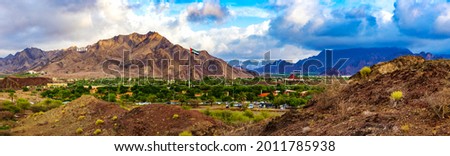Hatta city welcoming sign written with large letters placed in Hajar mountains and UAE flag flying high in Hatta enclave of Dubai in the United Arab Emirates.