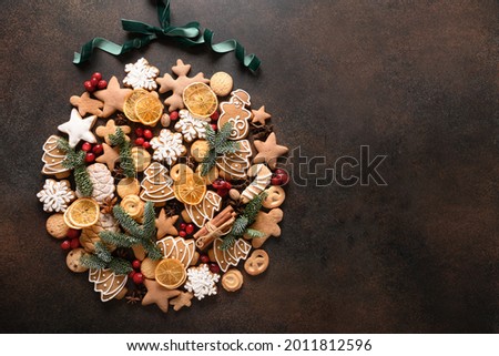 Creative Christmas ball of assorted cookies, cinnamon, anise stars, berries, orange chips, spruce branches on brown background. New Year greeting card. Top view. Xmas holiday background. Copy space.