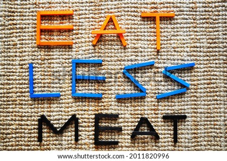 3D text in wooden blocks in orange, blue and black on jute carpet. It reads Eat Less Meat. Message in line with sustainability, climate action, climate change mitigation, reducing carbon footprint. Royalty-Free Stock Photo #2011820996