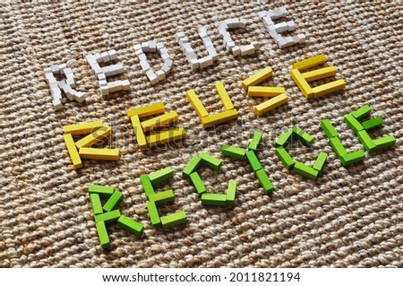 3D diagonal text in colored wooden blocks in white, yellow and green, on a jute carpet. It reads Reduce, Reuse, Recycle. Message for circular economy, sustainability, climate action, climate change. Royalty-Free Stock Photo #2011821194