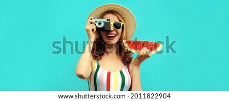 Summer portrait of happy smiling young woman with retro camera and slice of fresh watermelon wearing a straw hat on blue background