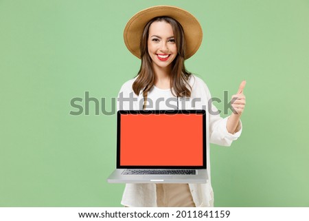 Traveler tourist woman in clothes hat camera hold laptop pc computer blank screen workspace show thumb up isolated on green background Passenger travel abroad on weekends. Air flight journey concept