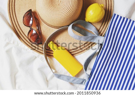 Flat lay photography beach essentials. Straw hat, stylish brown sunglasses, sunscreen cream, lemon and bag in white and blue stripes. Top view summer travel photo