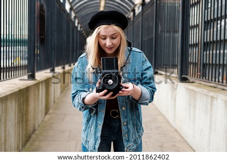 Young woman taking pictures with a medium format film camera. She is wearing a denim jacket and a black beret.