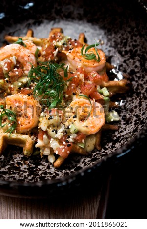 Zucchini waffles with tiger prawns on a black plate on a wooden table. Hot dish. Minimalism