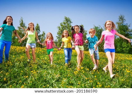 Happy children run and hold hands in green field