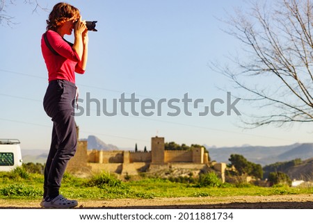 Mature female tourist with camera taking travel photos in Antequera city, Alcazaba fortress in the distance. Province of Malaga, Andalucia Spain.