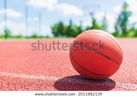 Orange old basketball ball on a red rubber court.Sunny summer warm day.Blurred background.Orange ball is waiting for the player.Copy space.