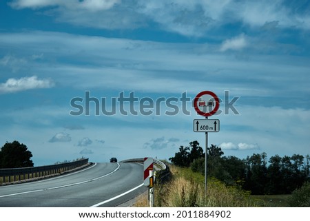 No overtaking sign. Road sign on the road in front of the bridge against the blue cloudy sky . High quality photo Royalty-Free Stock Photo #2011884902