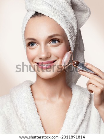 Beautiful woman using stone facial roller. Photo of woman with perfect skin on beige background. Beauty and skin care concept