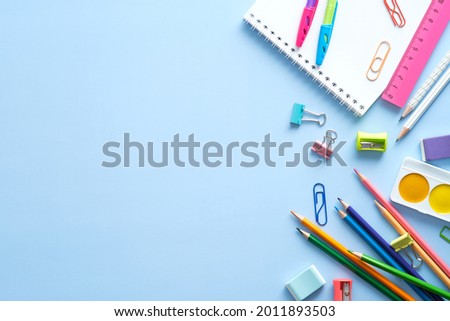 School stationery, color pencils, paints, notepad on blue table. Back to school background. Kids desk top view. Royalty-Free Stock Photo #2011893503