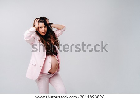 pregnant woman in pink suit close-up on gray background