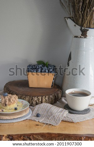 Fresh, farmhouse breakfast of sweat, yet tangy blueberry lemon muffins and strong, hot coffee. Live edge table. Antique picture with dried lavender. 