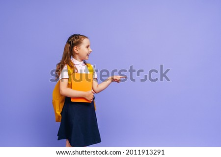 Cute happy baby in shape. he points his finger to the side on the purple background. child with backpack. the little girl is ready for school, going back to the conceptual school. the holidays begin.