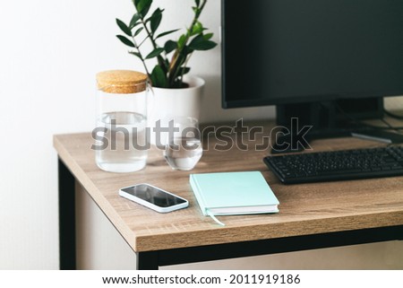 Workspace for IT worker with desktop, keyboard, notebook. phone, glass of water and a green plant