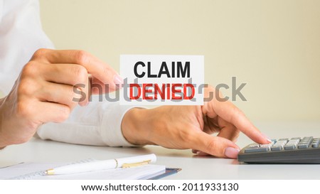 claim denied, message on business card shown by woman pressing calculator key at workplace in light office, selective focus, business and financial concept