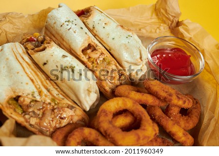 mexican burritos and onion rings with sauce on craft paper and yellow background.