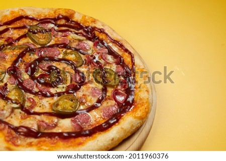 rustic pizza with sausages and jalapena on wooden board and yellow background.