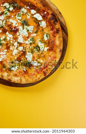 rustic pizza with feta cheese and herbs on wooden board and yellow background.