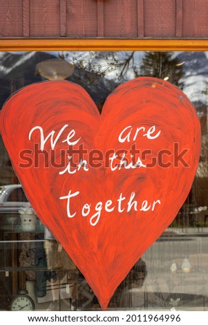 Red painting of a heart with We are in this together text on a window of the storefront 
