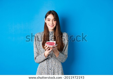 Beautiful girl holding birthday cake and celebrating, wishing happy bday and smiling, standing against blue background