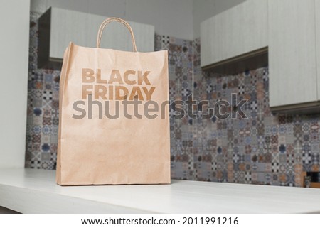 Cardboard bag written Black Friday on the table brown paper packaging with custom writing and kitchen in the background. Black friday concept. Product concept. Packaging concept. Copy space