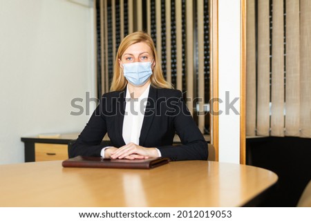 Business woman in protective mask sitting in her office at the negotiating table. High quality photo