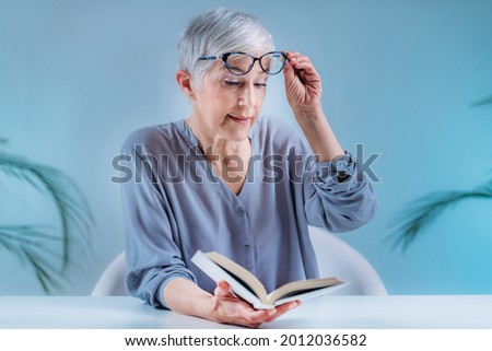 Senior woman with eyeglasses having problems with book reading. Indication for cataracts, glaucoma, and vision loss in the elderly. Royalty-Free Stock Photo #2012036582