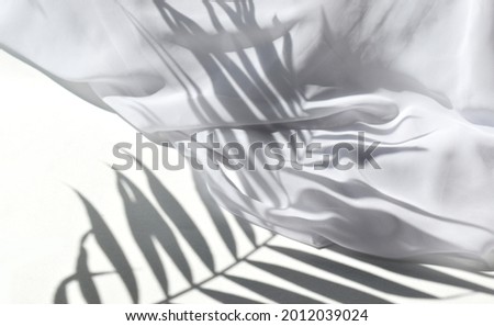 Summer sunlight still life mock up composition. White silk fabric on table in sunlit background. Palm leaves harsh shadows. Luxury minimal concept for wedding, resort vacation or spa products. Royalty-Free Stock Photo #2012039024