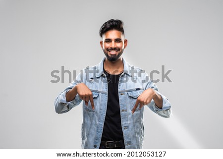 Shocked bearded male looks down with great disbelief, expresses surprisment and astonishment, indicate with fore fingers at floor, isolated over white concrete wall.
