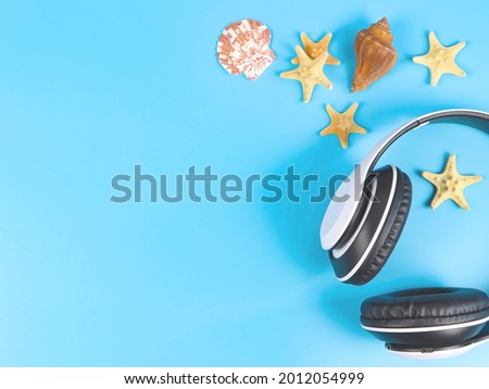 Top view or flat lay of white headphones with sea shells and starfishes on blue background, copy space. Summer beach background for music or podcast.