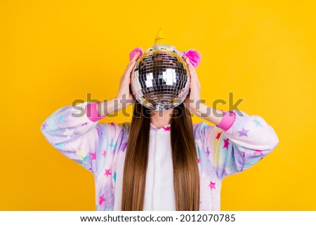 Portrait of attractive funny girl wearing kingurumi closing face shiny ball isolated over bright yellow color background