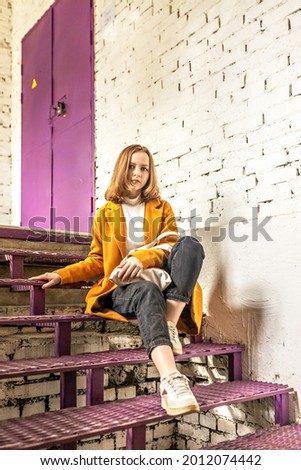 Portrait of a young teenage girl sitting on a purple staircase against a white brick wall.