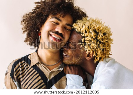 Affectionate young gay couple embracing each other while standing together in a studio. Two young male lovers smiling cheerfully while posing against a studio background. Gay couple being romantic. Royalty-Free Stock Photo #2012112005
