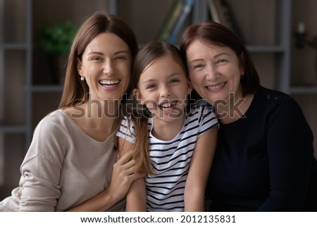 Family portrait of three female generations. Millennial mom, older grandma an preteen daughter kid hugging together, looking at camera, smiling, laughing. Intergenerational headshot