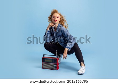 Disco, party time. Portrait of attractive woman in retro 90s fashion style, outfit isolated over blue studio background. Concept of eras comparison, beauty, fashion and youth. Royalty-Free Stock Photo #2012165795