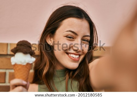 Young caucasian girl eating ice cream making selfie by the camera at the city.