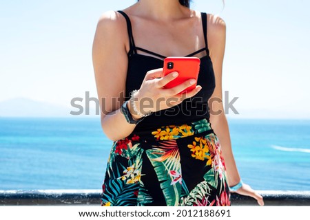 Hipster girl hold on smart phone gadget on sandy coast beach, Traveler waits and uses mobile in female hand on background seascape horizon. Tourist look in blue sun