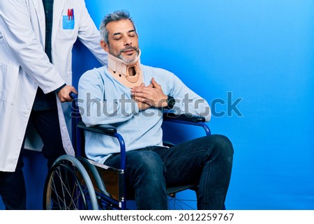 Handsome middle age man with grey hair on wheelchair wearing cervical collar smiling with hands on chest with closed eyes and grateful gesture on face. health concept. 